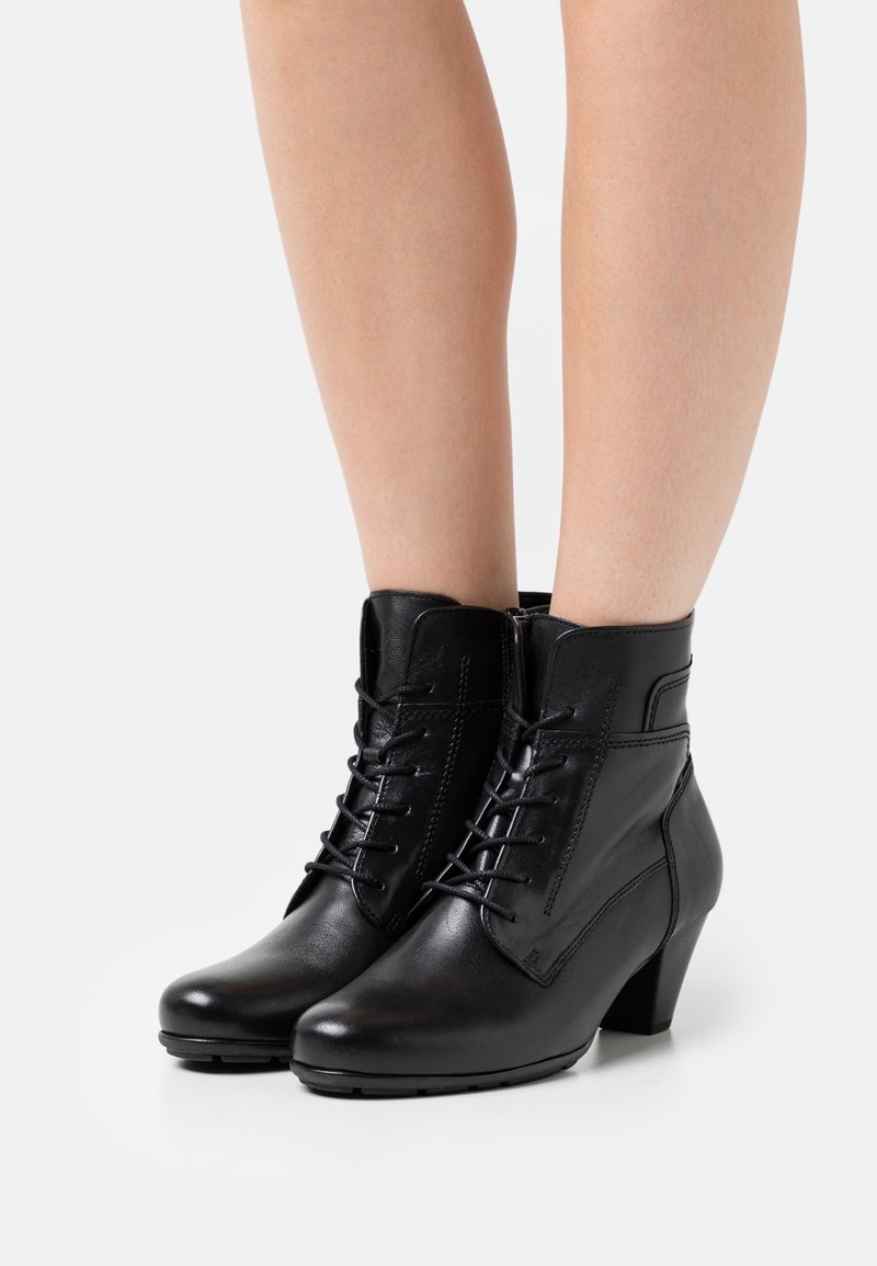 Botas de tobillo de cuero negro con un acabado suave, cordones en la parte delantera y un tacón ligeramente afilado. Detalles de costura en los lados.