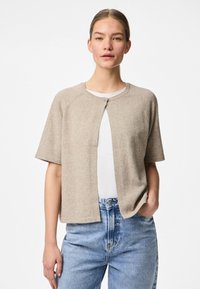 Cardigã bege de mangas curtas com decote redondo e fecho de botões, feito de um material suave, combinado com jeans de denim azul-claro.