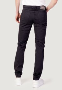 Pantalones de algodón negros con un corte ajustado, diseño de cinco bolsillos y una etiqueta en la cintura. Combinados con zapatillas blancas y una camiseta blanca lisa.