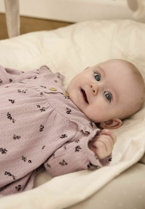Langärmliges, hellrosa Babykleid mit Rüschekragen, versehen mit einem Blumenmuster und zwei Holzknöpfen, auf einer weichen, cremefarbenen Oberfläche ausgelegt.