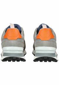 Grijze suède sneakers met een oranje leren hakaccent, witte tussenzool en gestructureerde zwarte rubberen zool. Achteraanzicht toont de ontwerpelementen.