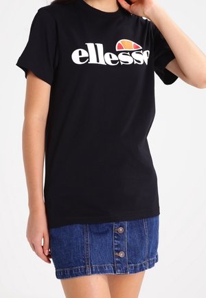 Schwarzes T-Shirt mit kurzen Ärmeln, weißem "ellesse"-Logo und einem orange-roten Halbkreis darüber, kombiniert mit einem blauen Jeansrock mit Knöpfen.