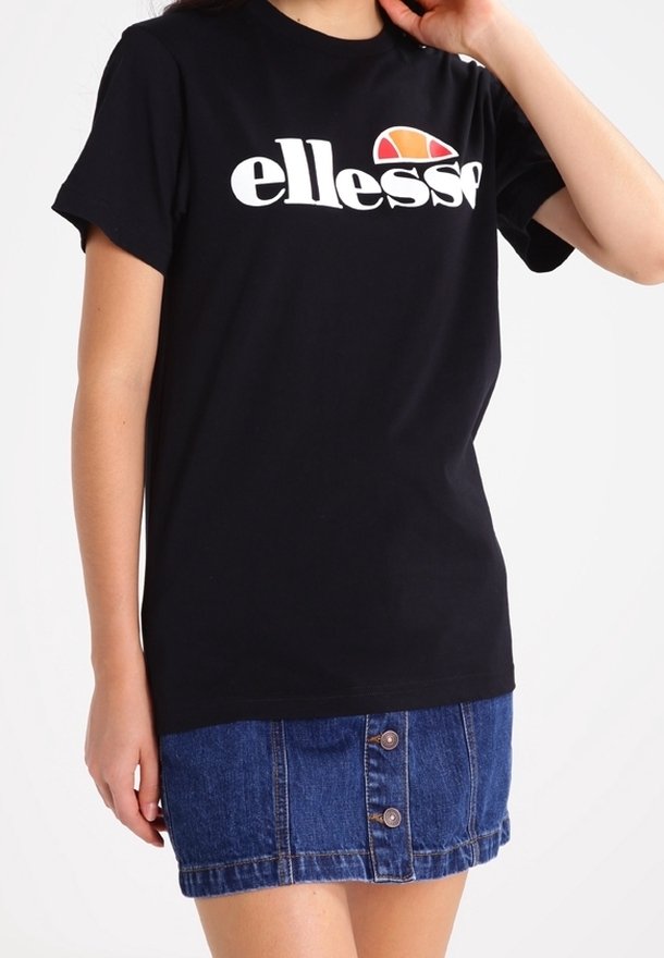 T-shirt noir à manches courtes avec le logo "ellesse" blanc et un demi-cercle orange-rouge au-dessus, associé à une jupe en jean bleue boutonnée.