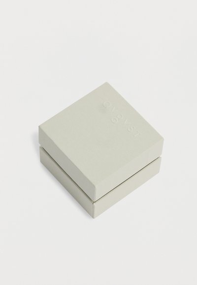 Κλειστό τετράγωνο κουτί ανοιχτό γκρι με ανάγλυφο λογότυπο "COVER STORY" στο καπάκι, τοποθετημένο σε λευκό φόντο.