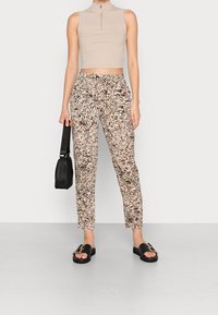 Haut court côtelé beige clair avec un col montant, associé à un pantalon à motifs beige et noir, et des sandales plates noires.