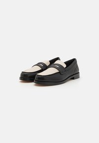 Mocassins noirs et crème avec une finition en cuir lisse et un détail de couture contrastant à l'avant. Conception à talon block bas.