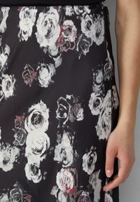 Jupe en tissu noir avec un motif floral de roses blanches et grises, avec des accents rouges subtils, texture lisse et silhouette droite.