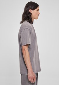 Tricou gri cu mânecă scurtă din bumbac moale. Are o croială relaxată, guler rotund și cusături vizibile pe margini.