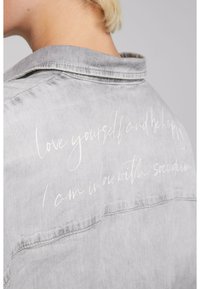 Gray denim jacket featuring a collar, with white text on the back reading "love yourself and be happy" and "I am in love with soco denim."