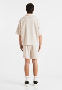 Crème-kleurig shirt met korte mouwen en bijpassende shorts, met een golvenpatroon. Draag het met zwarte sneakers en witte sokken.