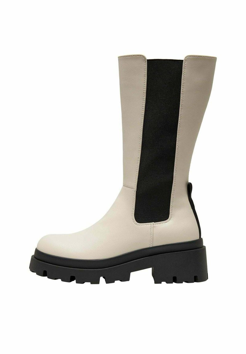 Stivali al ginocchio con un corpo in pelle crema e un pannello elastico nero. Suola nera spessa e texture, con scanalature profonde per una buona aderenza.