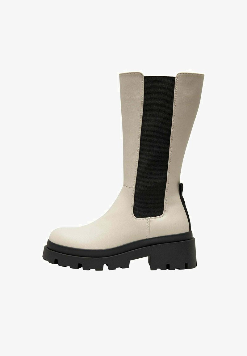 Stivali al ginocchio con un corpo in pelle crema e un pannello elastico nero. Suola nera spessa e texture, con scanalature profonde per una buona aderenza.