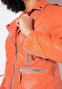 Orangene Leder-Motorradjacke mit mehreren Reißverschlusstaschen, einem Druckverschlusskragen und einem taillierten Design mit strukturierten Ärmeln.
