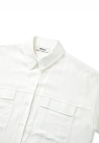 Camisa blanca de botones fabricada en tejido ligero, con un cuello clásico, dos bolsillos delanteros y una textura suave. Etiqueta de la marca: IPEKYOL.