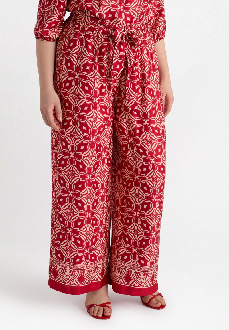 Pantalons larges à motifs rouges avec taille à nouer, présentant un design floral en crème et rouge, et un détail d'ourlet contrastant.