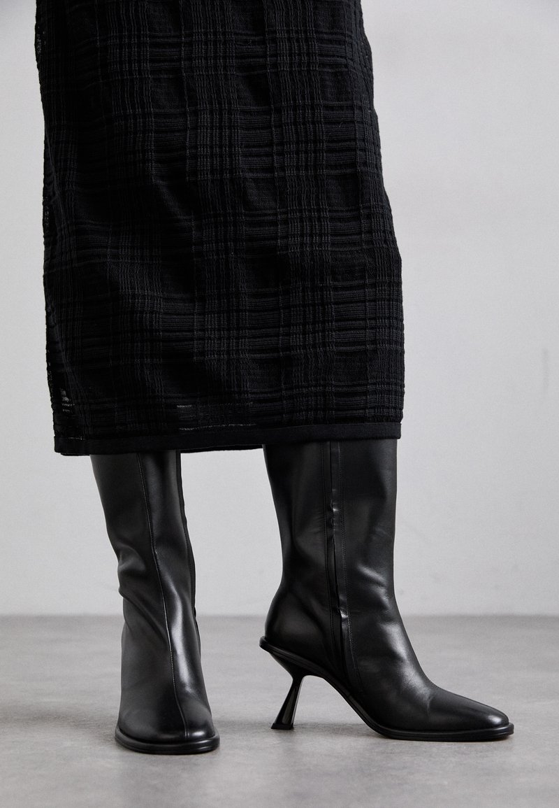 Svarta läderknähöga stövlar med spetsiga tår och smala stilettklackar. Slät textur med en figursydd design och subtila sömnadsdetaljer.
