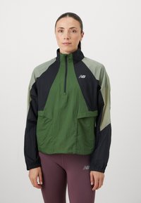 Veste coupe-vent en vert, noir et gris clair. Présente un col haut, une fermeture éclair et deux poches avant. Tissu léger.