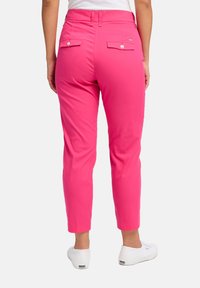 Roze katoenen broek met een slim fit, voorzien van twee achterzakken met knoopsluiting en een tailleband. Gecombineerd met witte canvas schoenen.