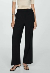 Schwarze weit geschnittene Hosen mit glatter Textur, mit einer maßgeschneiderten Passform, vertikalen Nähten und einer hohen Taille, kombiniert mit schwarzen Absatzsandalen.