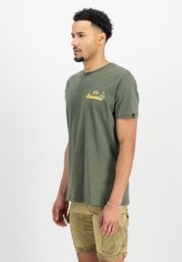 Oliven grøn bomulds t-shirt med gul "Hawaii" tekst og grafisk design. Korte ærmer; rund hals. Glat tekstur; afslappet pasform.