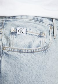Světle modré džíny z denimu s vybledlým efektem, s nášivkou cK na zadní kapse a detaily s kovovými knoflíky. Klasický design s pěti kapsami.