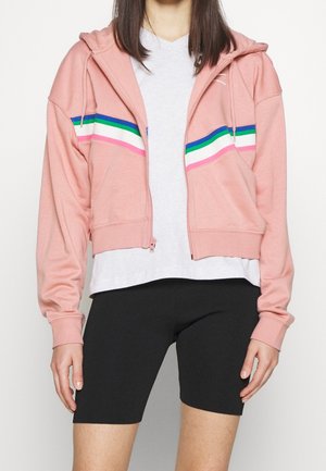 Pink cropped hoodie with a front zipper, featuring multicolor stripes across the chest. Paired with a gray shirt and black shorts.