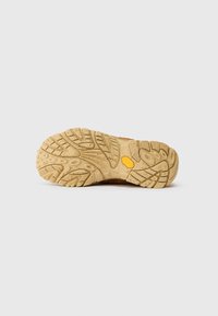 Gumová podrážka s texturovaným vzorem, obsahující hluboké drážky a logo Vibram. Barva je světle hnědá se skvrnitými akcenty.