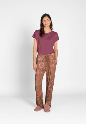 Woman standing wearing a purple striped short-sleeve shirt, brown floral print pants, and pink slippers on a white background.