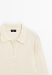 Svetle béžový vlněný polo svetr s knoflíkovým zapínáním, měkkou texturou a klasickým designem límce. Obsahuje pět Shodných knoflíků.