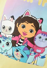 Camiseta gráfica con un personaje de dibujos animados con cabello rizado castaño y acentos en las orejas, rodeado de cinco gatos animados de colores. El fondo tiene un degradado en tonos pastel.