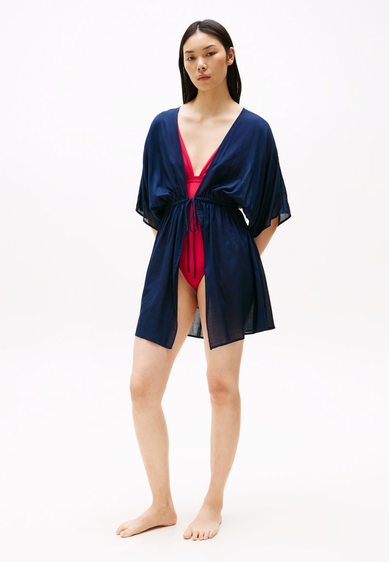 Kimono transparent de culoare bleumarin cu mâneci late, față deschisă și talie cu șnur, purtat peste un costum de baie roșu. Textură fină, design fluid și lungime până la genunchi.