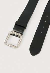 Musta nahkavyö, jossa on neliönmuotoinen hopeinen solki, koristeltu pyöreillä kirkkailla strasseilla; sileä pinta ja säädettävät reiät vyön varrella.