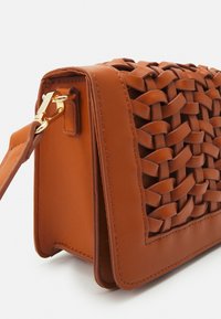 Bruine gevlochten leren tas met een gestructureerde vorm, voorzien van gladde accenten en een sluiting van goudkleurig metaal. Gestructureerd oppervlak met zichtbare stiksels.