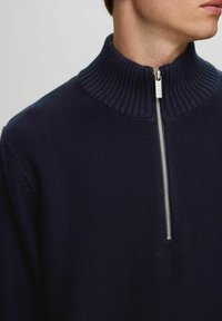 Marinblå stickad pullover med ribbad krage och silverfärgad dragkedja. Har ett strukturerat tyg och en avslappnad passform.