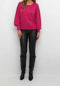 Pull fuchsia à manches longues et amples avec un col rond, associé à un legging en cuir noir taille haute et des bottes noires montant jusqu'aux genoux.