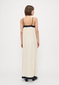 Rochie maxi cu un corp fluid de culoare crem și o bandă de sus de culoare bleumarin, cu bretele ajustabile. Materialul are un aspect ușor texturat.