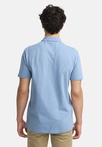 Lyseblå kortermet polo-skjorte med krage, laget av myk stoff, med rett kant og subtile sømdetaljer på baksiden.