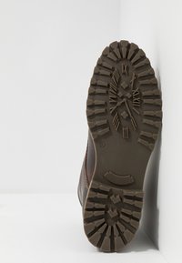 Bota de cuero marrón con una suela de goma robusta que presenta un diseño de profundidad para mejorar la tracción y un cuerpo liso con acentos de costura. Talla 42.