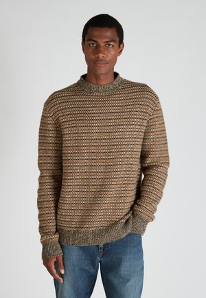 Braun- und cremefarbener gestrickter Pullover mit hohem Kragen, langen Ärmeln und gerippten Bündchen, kombiniert mit blauen Jeans.