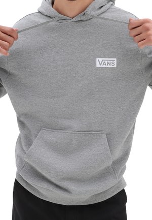 Persoon draagt een grijze Vans-hoodie, houdt de capuchonkoorden vast, met een voorzak in kangaroostijl en het Vans-logo op de borst.