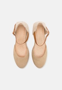 Zapatos de ante marrón con parte superior trenzada y correa de cuero. Presentan una punta redondeada y una plantilla texturizada con un patrón de hojas.