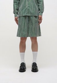 Set format dintr-o cămașă și pantaloni scurți cu dungi verzi și albe, având un design cu nasturi. Purtați cu șosete albe și pantofi cu talpă înaltă negri.