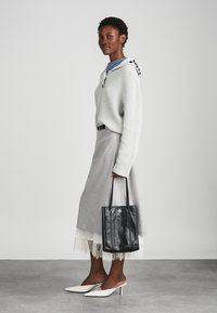 Pull en tricot gris clair avec capuche, associé à une longue jupe grise avec une finition en dentelle. Sac fourre-tout en cuir noir et talons aiguilles blancs.