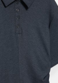 Tengerészkék poloing puha kötött anyagból, klasszikus gallérral és öt fekete gombbal ellátott patenttal, sima, texturált felülettel.