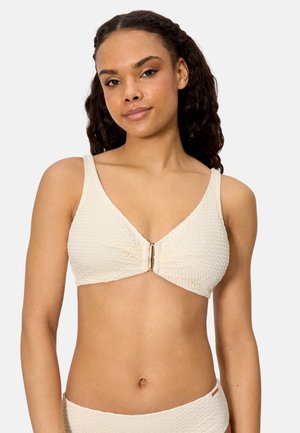 Mujer vistiendo un top de bikini texturizado color crema con un broche frontal y braga de talle alto a juego, sobre un fondo liso.