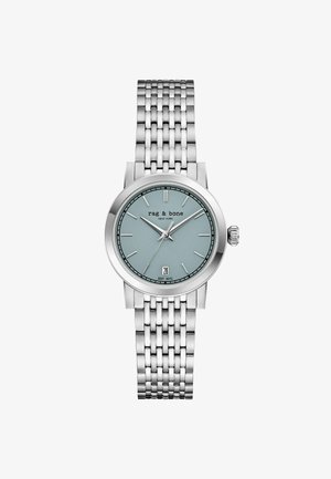 Zilveren metalen polshorloge met lichtblauwe wijzerplaat, slanke uurmarkeringen, datumvenster op 6 uur, en "rag & bone NEW YORK" tekst op de wijzerplaat.