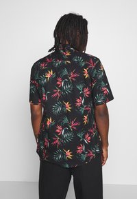 Zwart shirt met korte mouwen, voorzien van een levendig tropisch patroon met groene bladeren en roze accenten. Gemaakt van lichte stof met een gladde textuur.