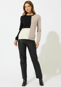 Maglione lavorato a maglia con un design a blocchi di colore in nero, crema e beige. Collo a giro, maniche lunghe e orlo a costine. Abbinato a pantaloni in pelle neri.