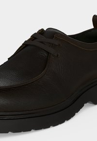 Σκούρο καφέ δερμάτινο casual παπούτσι με στρογγυλεμένη μύτη, μαύρη παχιά ελαστική σόλα και απλό σύστημα δέσιμου.