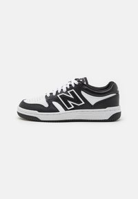 Baskets basses New Balance noir et blanc avec lacets blancs et semelle en caoutchouc, vues de côté sur un fond clair.
